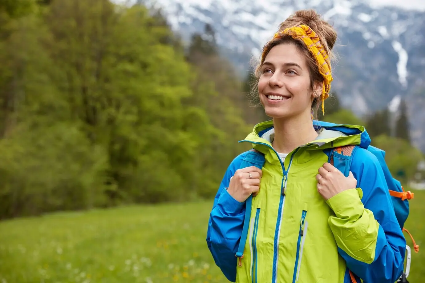 Horizontale Aufnahme einer glücklichen, unbeschwerten jungen Frau, die draußen vor der Kulisse einer Berglandschaft spaziert und es genießt, ihre Freizeit auf einer Wiese zu verbringen.